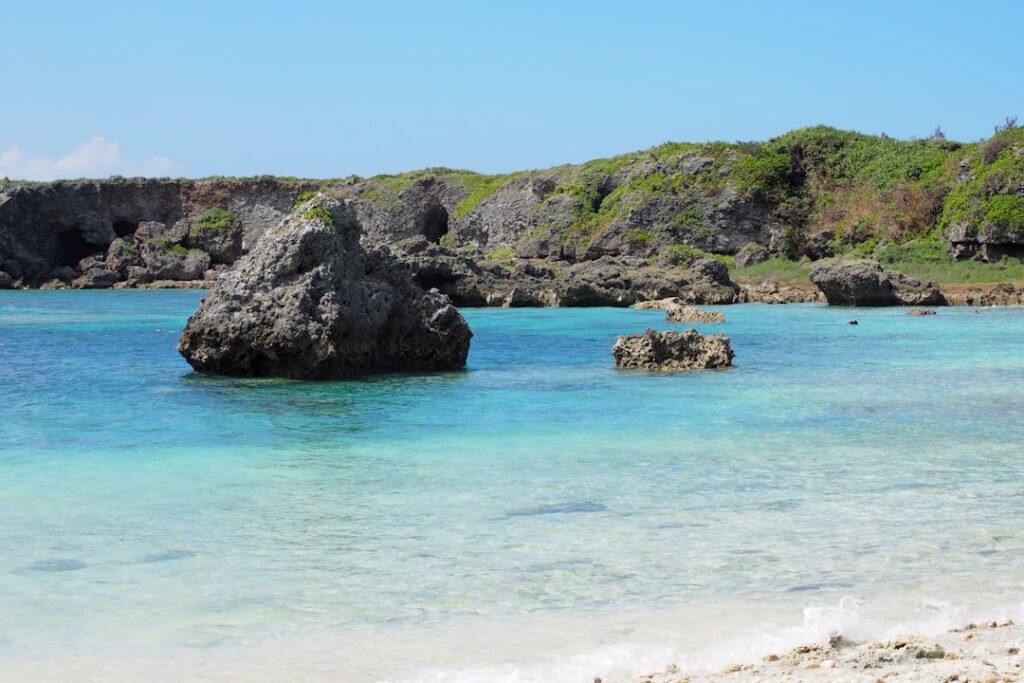 Turquoise shallow water and white sand beach in Okinawa with tropical vegetation along the shoreline.